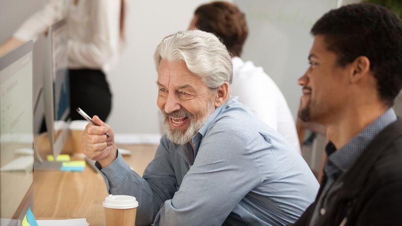 Smiling senior employee discussing email with colleague at workplace. Source: Shutterstock.