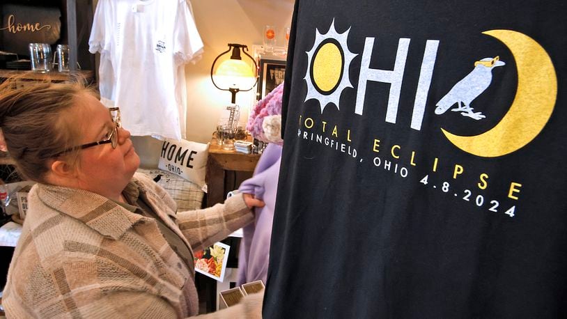 Jordan Lyons straightens a display at Champion City Guide and Supply Wednesday, March 20, 2024. The new total eclipse t-shirts, on sale at the downtown Springfield store, have quickly become very popular. BILL LACKEY/STAFF