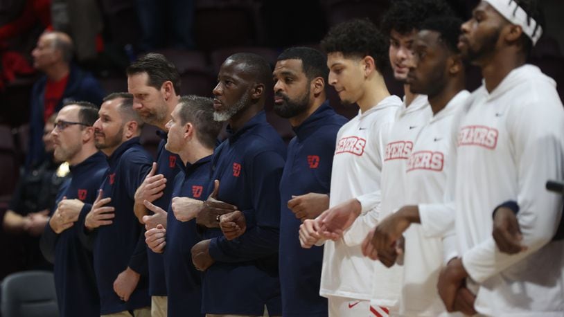 Dayton coaches, including Anthony Grant, and players stand for the national anthem before a game against Virginia Tech on Wednesday, Dec. 7, 2022, at Cassell Coliseum in Blacksburg, Va. David Jablonski/Staff