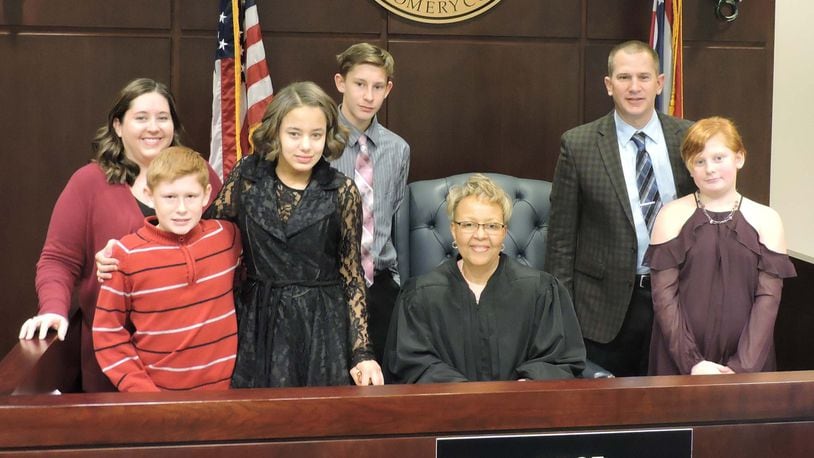 The Riggs family of Beavercreek Twp. formally adopted Kendal (third from left) on Dec. 15 at Montgomery County Probate Court. Pictured are (from left) Theresa, the mother; Tristan, age 11; Kendal, 14; Ian, 14; Judge Alice O. McCollum; Scott, the father; Rowan, 10. (Not pictured: Jacob, 16.) CONTRIBUTED