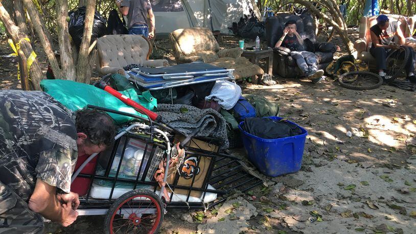 John Thomas, left, makes adjustments Sunday to a cart he planned to pull behind a bicycle to remove his possessions from a homeless tent camp behind Hamilton Plaza. MIKE RUTLEDGE/STAFF