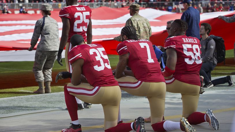SANTA CLARA, CA - NOVEMBER 6:  Quarterback Colin Kaepernick #7, safety Eric Reid #35, and linebacker Eli Harold #58 of the San Francisco 49ers kneel before a game against the New Orleans Saints with the U.S. flag unfurled in honor of the armed services on November, 6 2016 at Levi's Stadium in Santa Clara, California.  The Saints won 41-23. (Photo by Brian Bahr/Getty Images)