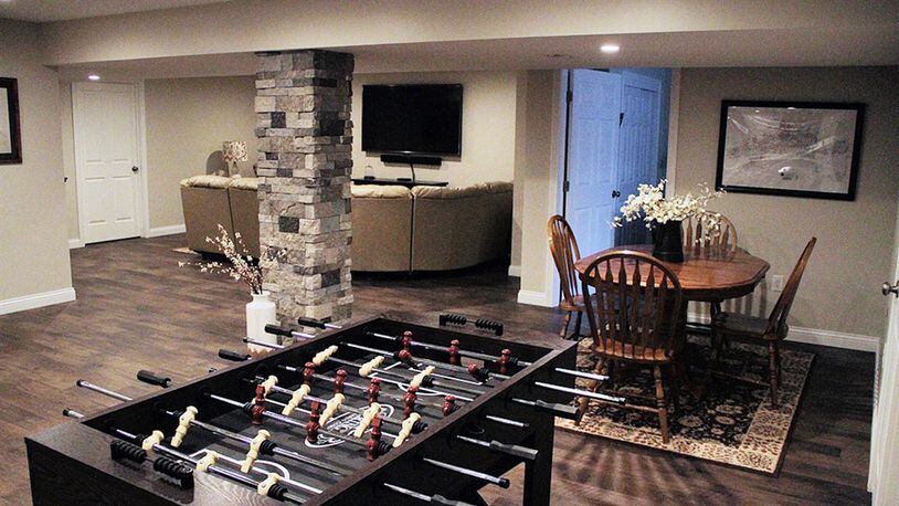 Earth-toned stone tile covers the square column at the center of the lower level’s open recreation space and is repeated in the backsplash area at the wine bar. There is plenty of space for game tables, and dedicated sitting/theater area is arranged at the end.