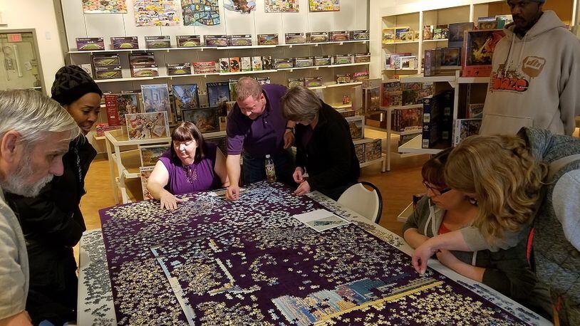 Virgil Chenoweth (from left), Jackie Givens, Cindy Chenoweth, Steve Nordmeyer, Lisa Nordmeyer, Diane Chenoweth, Kim Lever and David Givens tackle a 32,000-piece puzzle at Puzzles Plus at The Greene in Beavercreek. CONTRIBUTED