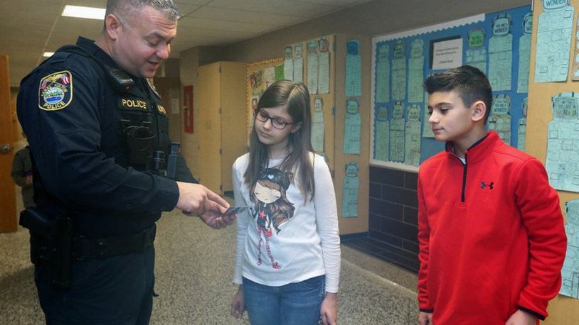 Canal Fulton Police Officer Dennis Muntean hands a “cop card” to Stinson Elementary School fifth graders Lana Storesina and Landon Kieffer on Wednesday, Jan. 24, 2018, in Canal Fulton. PHIL MASTURZO/THE AKRON BEACON JOURNAL
