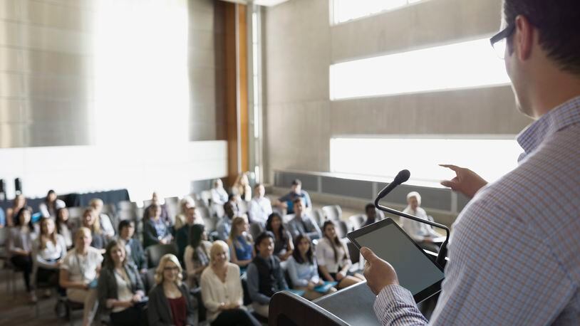 Professor with digital tablet speaking to students in auditorium (stock photo)