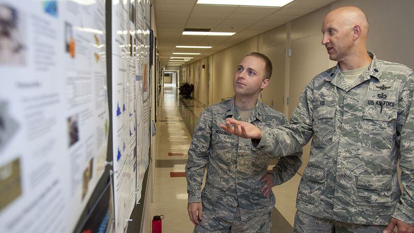 Lt. Col. James Fee, Air Force Institute of Technology assistant professor of nuclear engineering, discusses electromagnetic pulse and how to model it from a nuclear weapon with 1st. Lt. Cameron Merriman, an AFIT student, June 22 using a display board hung in one of AFIT’s corridors. (U.S. Air Force photo/John Harrington)