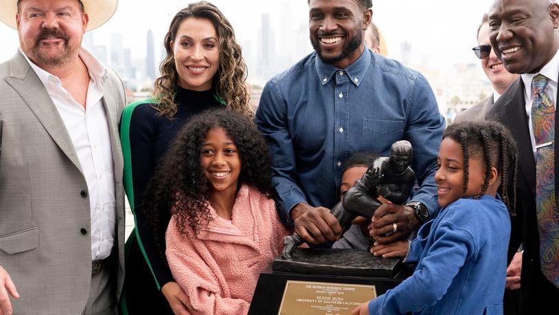 Former USC football player Reggie Bush poses with his attorneys, left, Levi McCathern and Ben Crump, right, along with his and family and his Heisman trophy during a news conference at the Los Angeles Memorial Coliseum, Thursday, April, 25, 2024, in Los Angeles. (AP Photo/Richard Vogel)