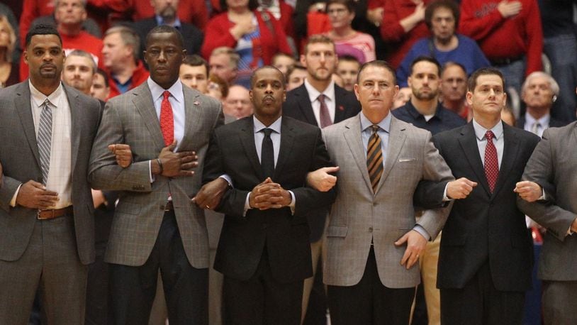 Dayton coaches (left to right) Ricardo Greer, Anthony Grant, Anthony Solomon, Donnie Jones, Darren Hertz and Andy Farrell stand during the national anthem before a game against Purdue Fort Wayne on Friday, Nov. 16, 2018, at UD Arena. David Jablonski/Staff
