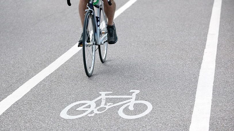 Commuter riding a bicycle on a city cycle lane or path across white painted bike symbol