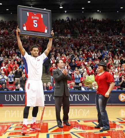 Dayton senior Devin Oliver, left, holds up a framed jersey on Senior Night as coach Archie Miller and Oliver's sister Miya applaud before a game against Richmond on Saturday, March 8, 2014, at UD Arena. David Jablonski/Staff