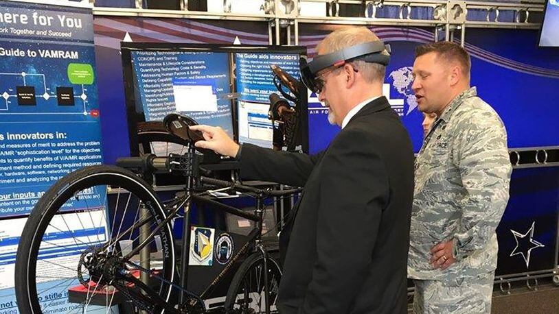 Dr. Michael Gregg (left), director of the Air Force Research Laboratory Aerospace Systems Directorate, uses a mixed-reality application to change the tire on a Wright Cycle Company bicycle as Capt. David Eisensmith guides the process. The demonstration, on display at the 2019 Air Vehicles Technology Symposium, is part of the Virtual, Augmented and Mixed Reality for Aircraft Maintenance team’s effort to show the technology’s potential for future aircraft maintenance. (Courtesy photo)