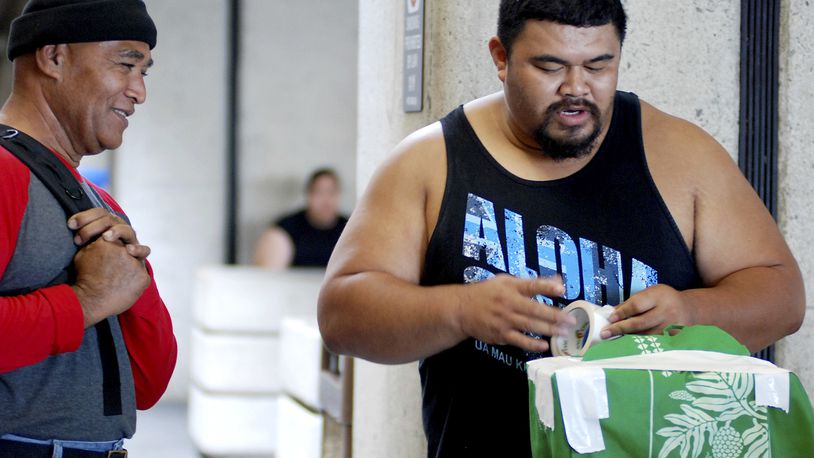 In this Oct. 10, 2016 photo, Mua Migi, left, watches his son Atimua Migi put tape on a carry-on bag before boarding a Hawaiian Airlines flight to Pago Pago, American Samoa at Honolulu International Airport in Honolulu. Atimua Migi doesn't like the airline's new policy of assigning seats at the airport after the airline conducted a survey that involved weighing passengers traveling between Pago Pago and Honolulu. (AP Photo/Jennifer Sinco Kelleher)