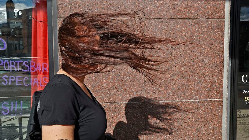Tish Molina's face is obscured by her hair as it blows in the wind Thursday, Feb. 9, 2023 as she walks along Main Street in Springfield. Wind gusts were measured up to 60 mph in the region Thursday. BILL LACKEY/STAFF