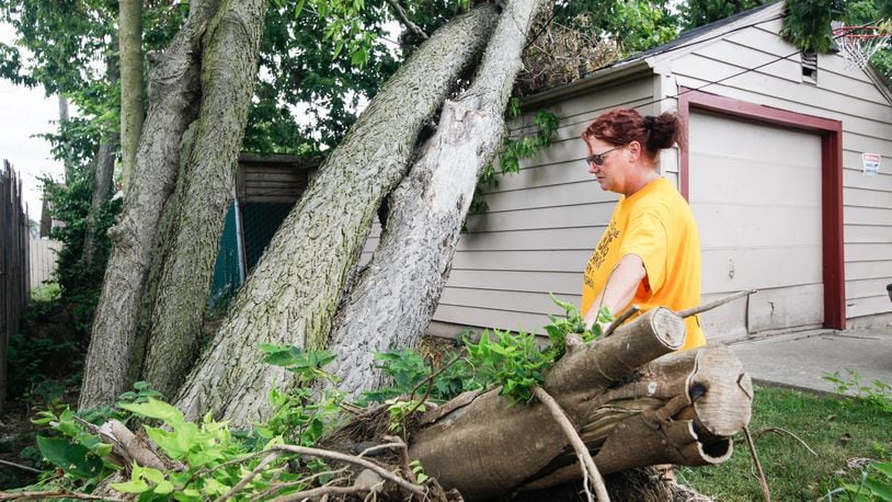 A large tree continues to lean precariously over Nicole Sapp’s garage behind her Brandt Street home in Dayton. She and husband David got bids to have it removed, but the lowest at $2,000 was still more than the family of six can afford right now, she said. “It’s just going to sit there. I don’t know what to do with it,” she said. CHRIS STEWART / STAFF