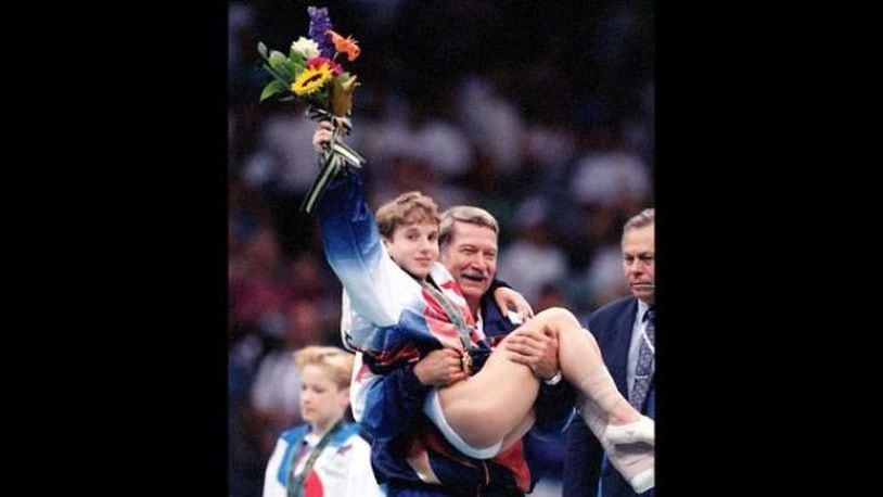 Kerri Strug hoists her flowers to the cheering crowd as she is carried from the podium by team coach, Bela Karolyi at the Georgia Dome on Tuesday, July 23, 1996. (Photo by Skip Peterson / Dayton Daily News)