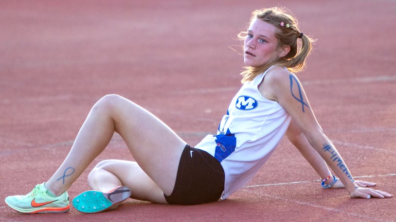 Miamisburg junior Lauren Zanotelli rests after winning the 3,200 meters at Friday's Division I regional  meet at Wayne. She and her teammates drew blue ribbons on their arms and legs in memory of head coach Melvin Johnson. Zanotelli also wrote #4melvin on her left arm. Jeff Gilbert/CONTRIBUTED