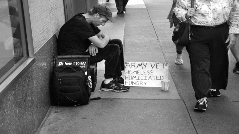 A man sits on a busy New York City sidewalk with a sign declaring he is a homeless military veteran.