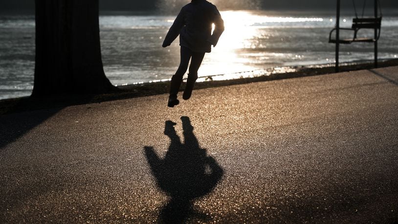 A young girl is silhouetted in the evening sun as she skips along the roadway in Snyder Park Tuesday to catch up to her father. BILL LACKEY/STAFF