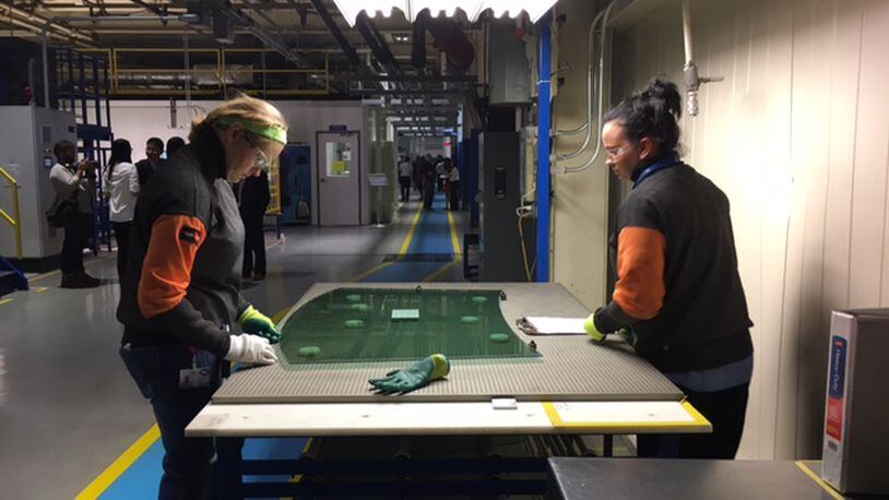 Two Fuyao Glass America workers inspect a sheet of glass earlier in October. The company wants to fill 200 production openings quickly. THOMAS GNAU/STAFF