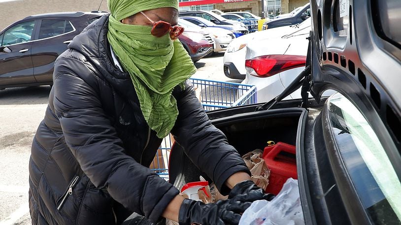 Ernnee Webber wears a scarf over her head and face and gloves as she puts her groceries in the trunk of her car Friday at Meijer in Springfield. Webber said she tried to find some medical masks but every place was sold out, so she made her own. BILL LACKEY/STAFF