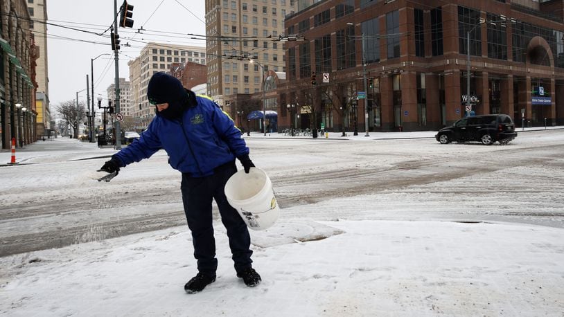 Downtown Dayton Partnership Ambassador Kalez Crise spreads ice melt on downtown sidewalk at Third and Main streets.
