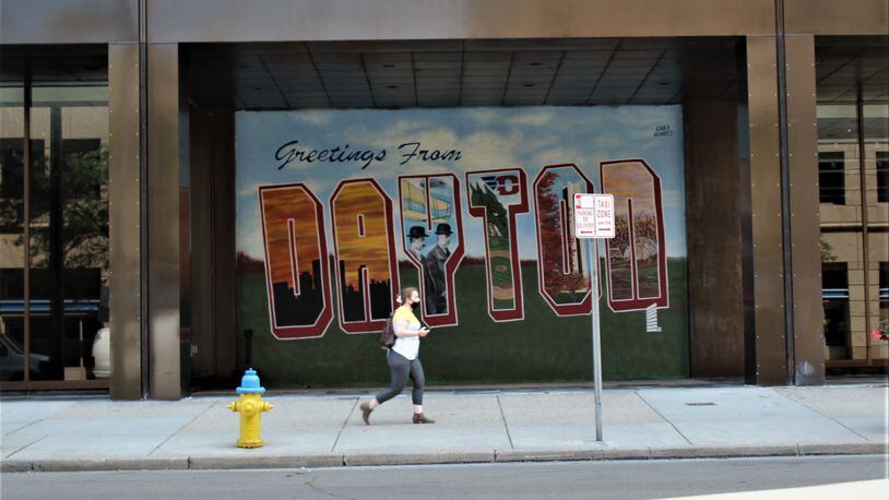 A woman on her cell phone walks past a Dayton mural in downtown. CORNELIUS FROLIK / STAFF