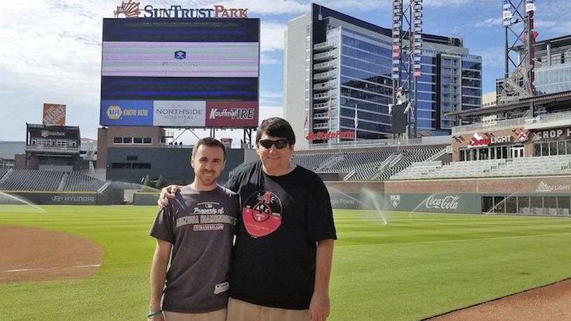 In this 2017 photo provided by Frank Gennario Jr., Frank Gennario Jr. and his son, Tony, pose at SunTrust Park in Atlanta.  Frank Gennario lost his father to bone cancer when he was 16, and he clings tightly to memories of their days at Yankee Stadium. When Frank's only son was nearing the same age, it became critical to him that they build those same ballpark memories. So the pair set a goal: see their beloved Arizona Diamondbacks play in every big league park. Ten years later, they have completed their quest. (Frank Gennario Jr. via AP)
