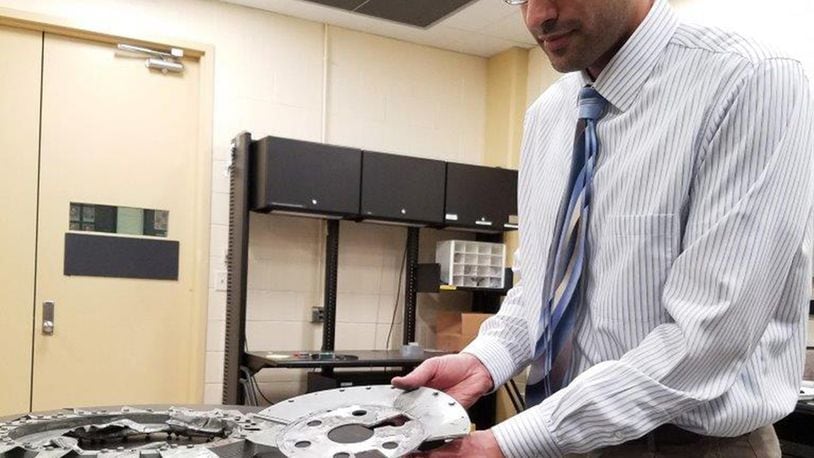 Air Force Research Laboratory Materials and Manufacturing Directorate engineer Alan Oquendo demonstrates the failed flywheel assembly and engine cooling fan that resulted in a non-injury incident involving the Wright “B” Flyer replica aircraft. Oquendo and the Materials Integrity Branch Structural Materials Evaluation team uncovered critical evidence that explained the event and recommend an improved design. (U.S. Air Force photo/Holly Jordan)