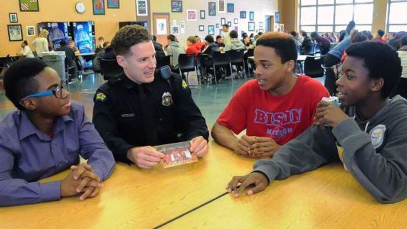 Police officer Zach Hastings and Belmont High School students (from left) Seth Burdette, Kenyon Evans and Billy Veal look at photos of basketball players and discuss scrimmage. JENNIFER BRYANT/CONTRIBUTED
