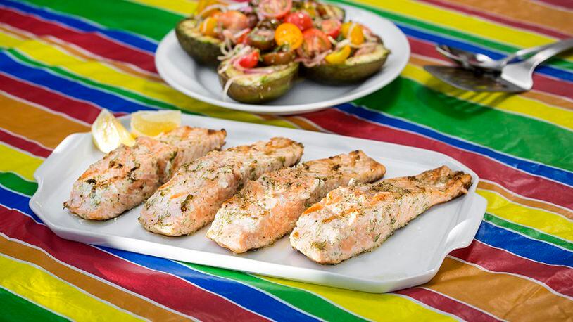 Grilled salmon on the table. The salmon were brushed with dill mayonnaise, accompanied by grilled avocado halves brushed with mayonnaise, salt and pepper, then topped with marinated tomato salad. (Ricardo DeAratanha/Los Angeles Times/TNS)