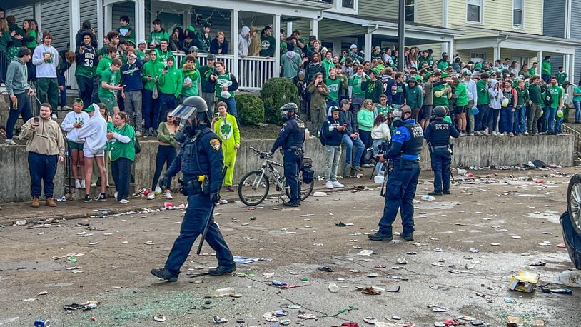 Police officers are shown on littered streets as crowds gather on sidewalks and yards after a party turned into a disturbance on Saturday, March 25, 2023. Some people overturned a vehicle, and at least six people were arrested, according to university officials. KEEGAN GUPTA/CONTRIBUTED