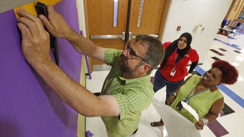 Dayton Public Schools teachers prepare a bulletin board in the Boys Prep Academy on Friday afternoon. Jeff Theis, left, Sophia Shalash and Alva Johnson, right, were busy preparing for classes to begin on Tuesday, August 15. TY GREENLEES / STAFF