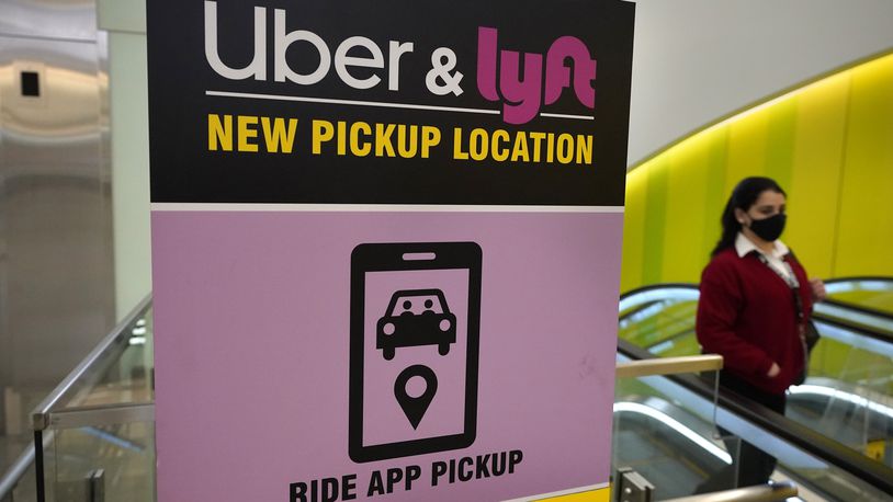 FILE - In this Feb. 9, 2021 file photo, a passer-by walks past a sign offering directions to an Uber and Lyft ride pickup location at Logan International Airport, in Boston.