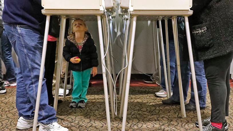 A 4-year-old girl plays under the voting booths as her mother casts her vote Tuesday. BILL LACKEY/ STAFF