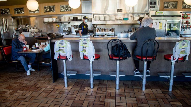 Kim Kaseta (L) waits for her pattie melt while sitting at the counter at the Waffle House in Brookhaven on Monday, when Georgia restaurants were allowed to have customers dine in again. The bags covering the chairs marked where customers weren’t allowed to sit in order to keep some social distancing. STEVE SCHAEFER / SPECIAL TO THE AJC