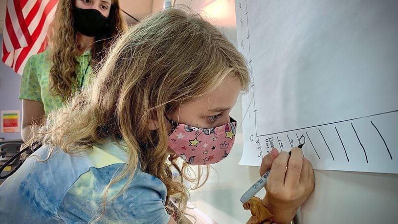Virginia Stevenson Elementary School third-grader Temperance Breehe does work on the board under the watchful eyes of teacher Tessler Baird on the first day of school, Tuesday, Sept. 7, 2021. MARSHALL GORBY\STAFF
