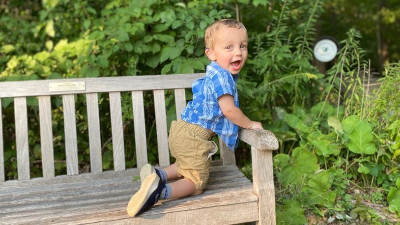Thomas Harris, two years old, climbs on a park bench looking back excitedly at the camera.