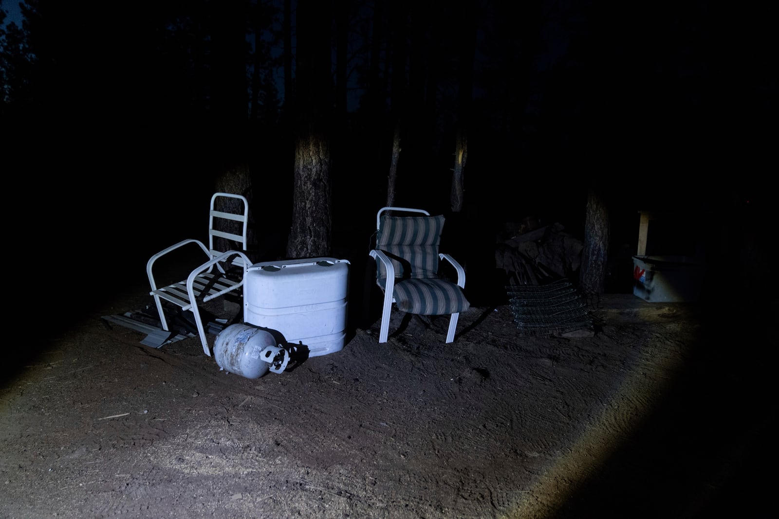 A flashlight from Mandy Bryant's shines on chairs propped up by trees at a homeless encampment in Deschutes National Forest Wednesday, April 30, 2025 near Bend, Ore. (AP Photo/Jenny Kane)