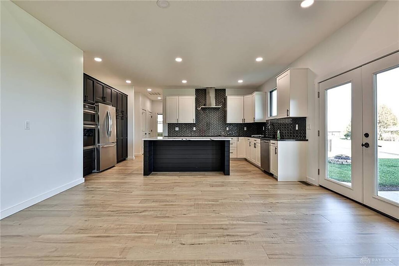 The open concept kitchen has an island with bar seating, quartz countertops and white cabinets and an exterior door opening to the covered back patio. CONTRIBUTED