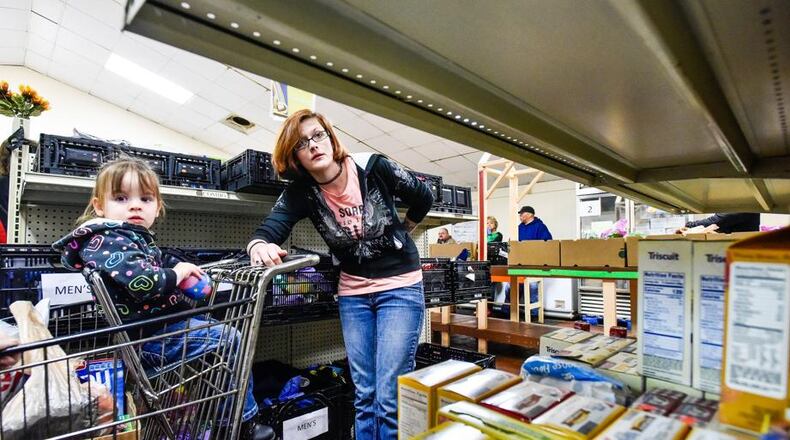Montana Sweezy, with her daughter Aurora, 2, loads a cart with food at Family Service of Middletown. Sweezy said even though she and her husband work full-time jobs it is hard to make ends meet and sometimes needs help providing food for her family. NICK GRAHAM/STAFF