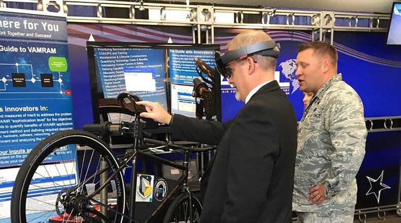 Dr. Michael Gregg (left), director of the Air Force Research Laboratory Aerospace Systems Directorate, uses a mixed-reality application to change the tire on a Wright Cycle Company bicycle as Capt. David Eisensmith guides the process. The demonstration, on display at the 2019 Air Vehicles Technology Symposium, is part of the Virtual, Augmented and Mixed Reality for Aircraft Maintenance team’s effort to show the technology’s potential for future aircraft maintenance. (Courtesy photo)