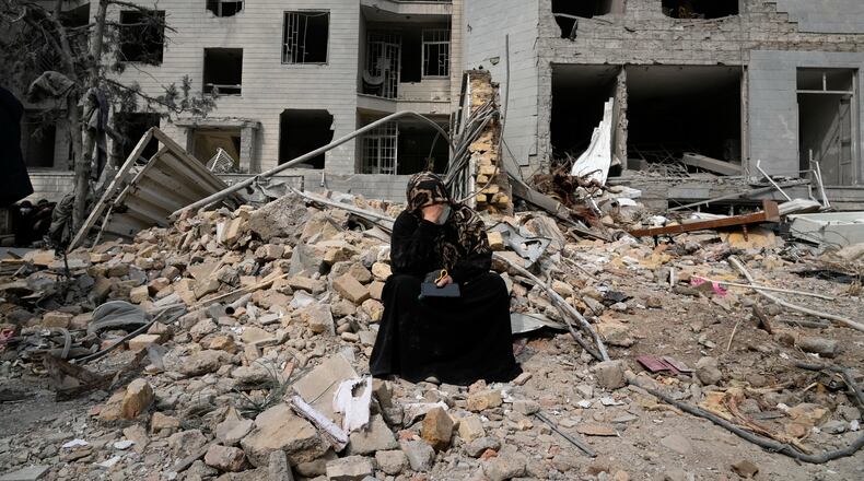 A woman sits on rubble across from a residential building damaged last Sunday during the U.S.-Israeli air campaign in Tehran, Iran, Thursday, March 12, 2026. (AP Photo/Vahid Salemi)