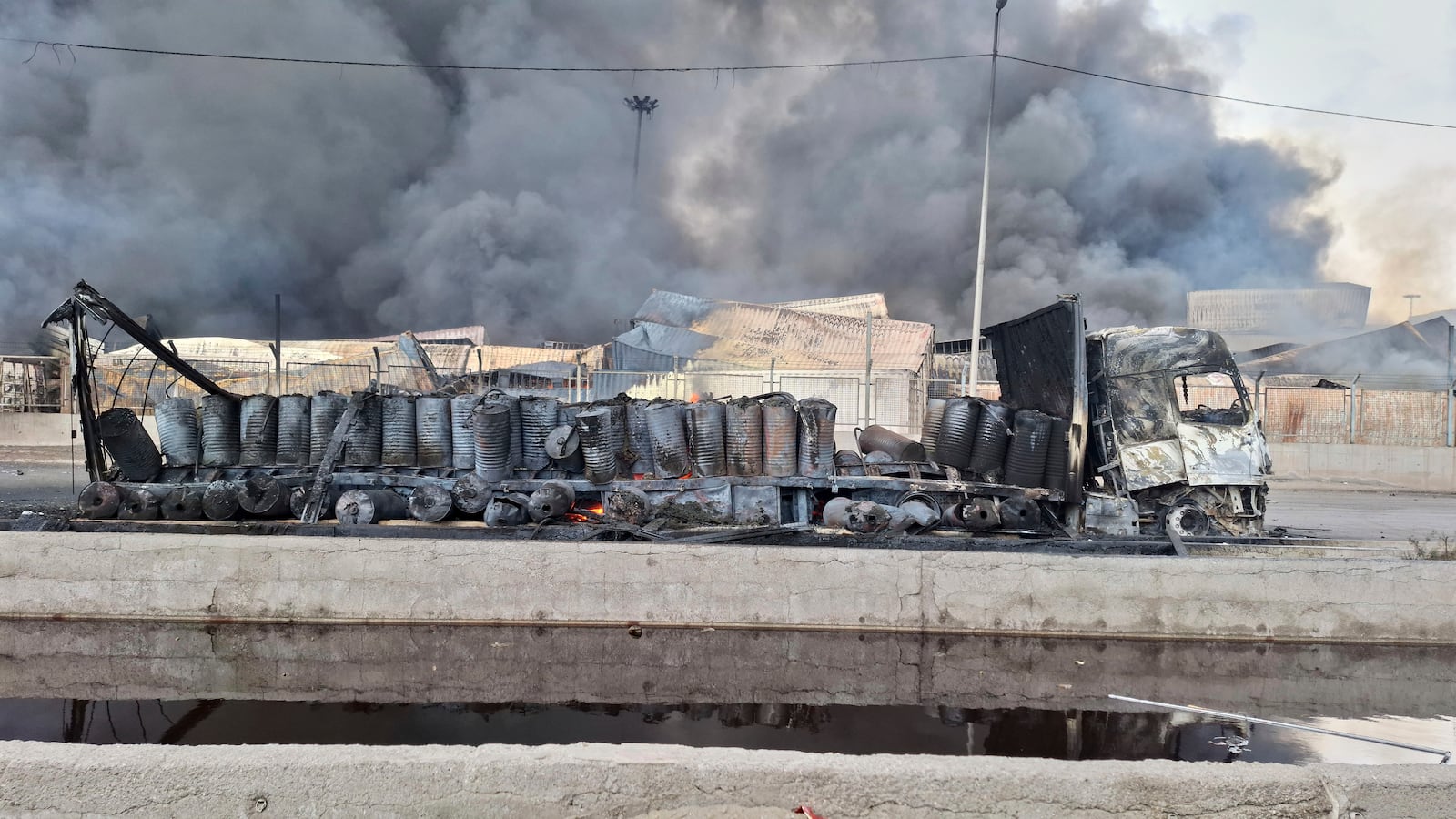 Smoke rises in background next to the gutted remains of a truck, Sunday, April 27, 2025, after a massive explosion and fire rocked a port near the southern port city of Bandar Abbas, Iran on Saturday. (AP Photo/Meysam Mirzadeh/Tasnim News)