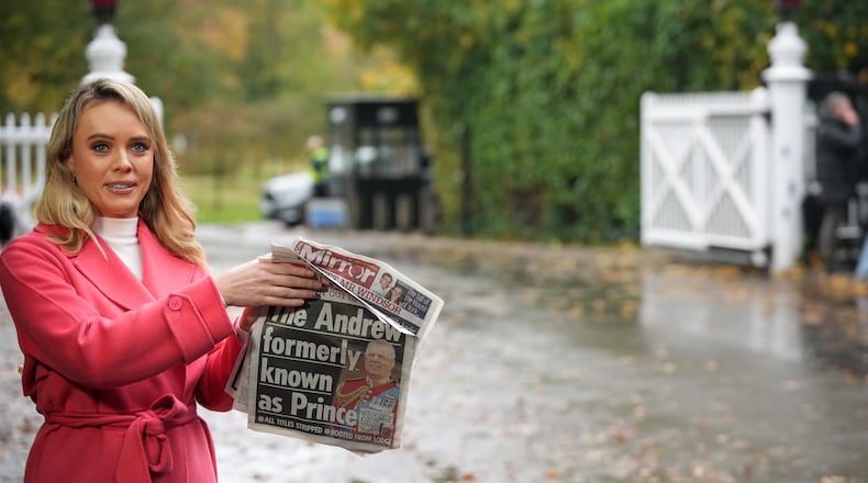 A TV presenter holds a newspaper with a picture of prince Andrew as she talks to the camera at a gate near to the Royal Lodge, following the announcement that Prince Andrew will be stripped of his titles and leave the 30-room mansion he has occupied for more than 20 years in Windsor, England, Friday, Oct. 31, 2025.(AP Photo/Alastair Grant)
