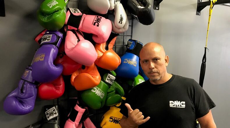 Daniel Meza-Cuadra stands next to boxing gloves hung on wall in his DMC Boxing Academy & Fitness on Miamisburg-Centerville Road. Tom Archdeacon/CONTRIBUTED
