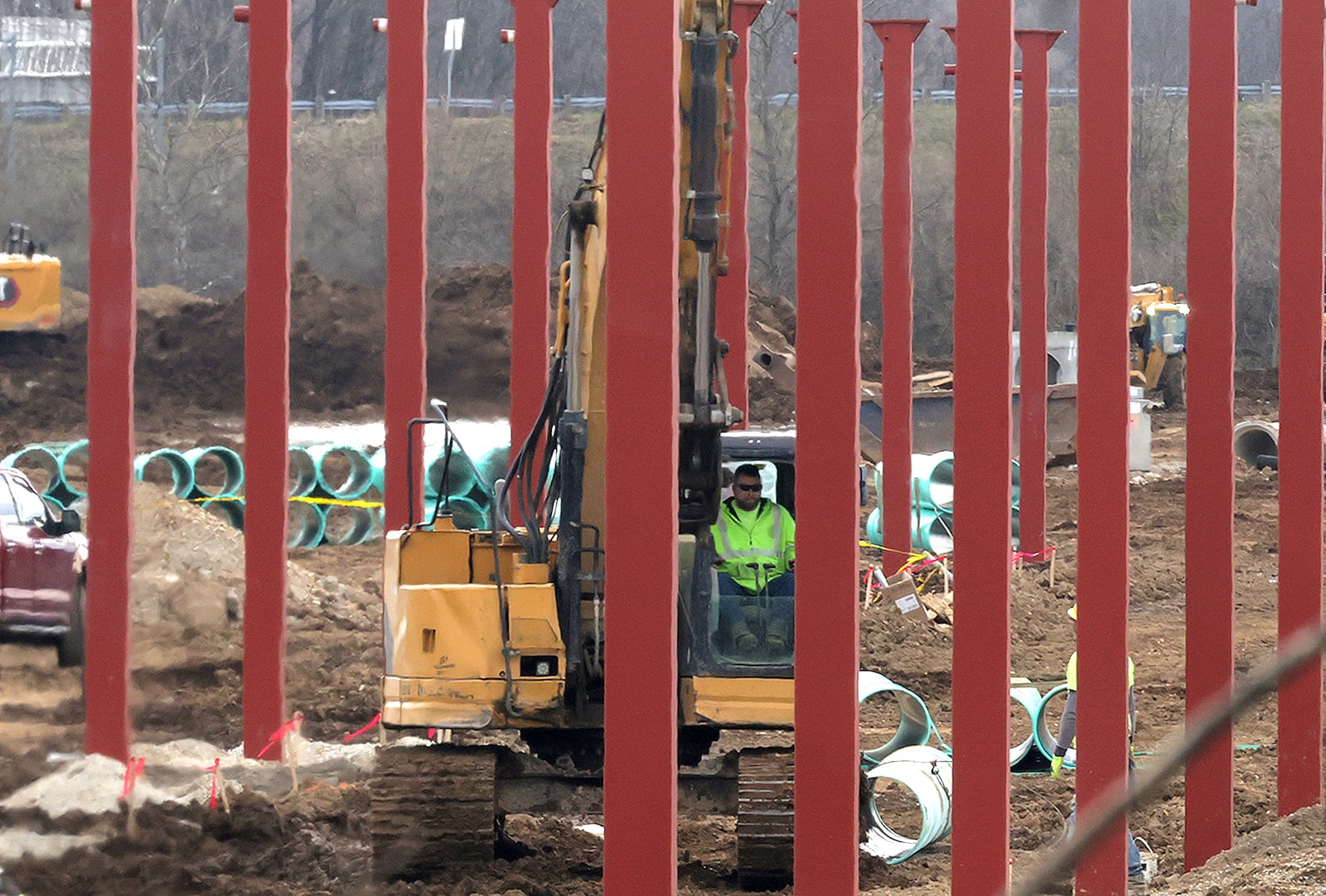 A construction worker driving an excavator is framed by the dozens of steel beams that have been placed as the supports for the gas pump awning at the new Buc-ees travel center at the intersection of Interstate 70 and Ohio Route 235 Tuesday, March 25, 2025. BILL LACKEY/STAFF