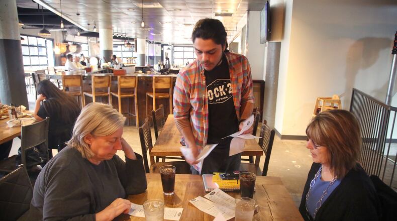 Louis Connelly, a bartender at Lock 27 Brewing in downtown Dayton, hands one-time use paper menus to guests Wednesday. The disposable menus are a response to the concerns about the coronavirus. The restaurant has also removed communal salt and pepper shakers and mustard and ketchup bottles from the tables and offers plastic cups and cutlery. LISA POWELL / STAFF