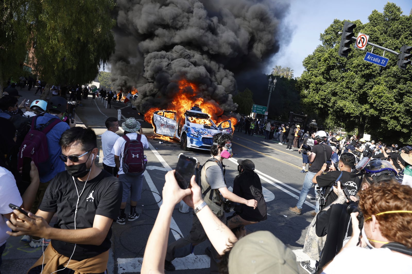 People watch while several Waymo cars burn in downtown Los Angeles after being vandalized by protesters reacting to a series of immigration raids that occurred in Los Angeles, Calif., on Sunday, June 8, 2025. (Stephen Lam/San Francisco Chronicle via AP)