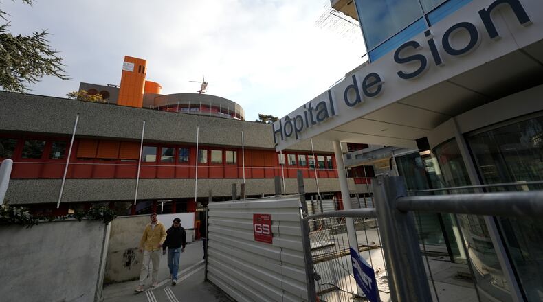 Two men walk outside a hospital as a helicopter takes off in Sion, Switzerland, Friday, Jan. 2, 2026, following the fire at the "Le Constellation" bar and lounge in Crans-Montana, Switzerland during the New Year celebration. (AP Photo/Baz Ratner)